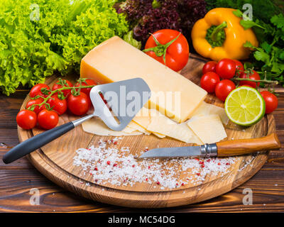 Vue d'en haut. planche en bois avec fromage parmesan, tomates cerises fraîches, de la laitue, sel de mer, de la chaux, le paprika et le poivre. bulgare rouge Le couteau pour couper v Banque D'Images