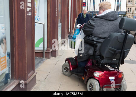 Un individu utilisant un scooter de mobilité sur un trottoir de ville occupé — accessibilité et indépendance dans un environnement urbain Banque D'Images