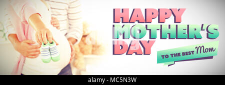 Composite image d'un brillant pregnant woman holding baby shoes tout en touchant son mari Banque D'Images