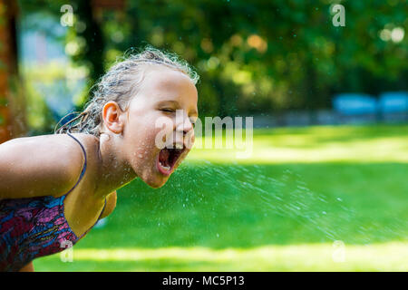Jeune fille attraper les gouttes d'eau de jardin arroseur. Banque D'Images