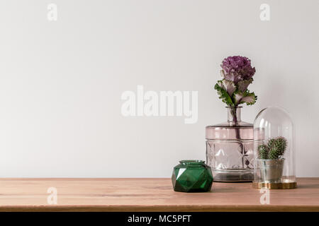 Gros plan d'une fleur dans un vase en verre rose et d'un petit cactus dans un dôme sur le côté de la surface en bois et un vide, fond blanc Banque D'Images