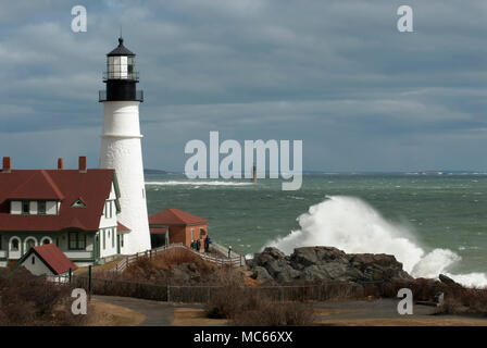 Les vagues déferlent sur les rochers géants par Portland Head Lighthouse et à Ram Island Ledge light comme soleil brise sotrm nuages dans le Maine. Banque D'Images