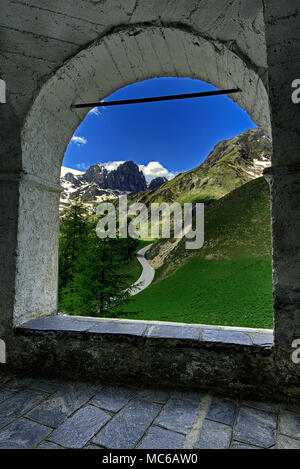 Vue de l'Alpes Cozie grâce à un arc du portique entourant le sanctuaire de San Magno (1761 m d'altitude), le Castelmagno, Val Grana, Piémont, Italie. Banque D'Images