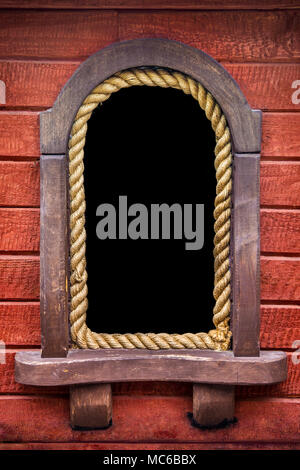 Close-up d'un hublot de bateau rouillé arrondis avec une corde de bois contre l'arrière-plan. Banque D'Images