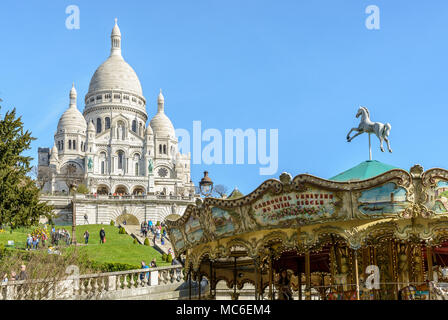 Vue sur la basilique du Sacré-Cœur en haut de la colline de Montmartre, avec vue sur le parc Louise Michel, avec un carrousel vintage au premier plan. Banque D'Images