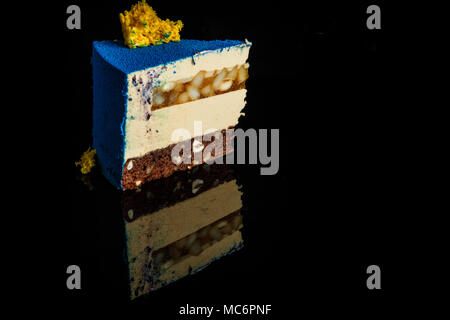 Morceau de gâteau mousse bleu avec décoration gâteau éponge jaune en haut et poire caramel couche se dresse sur fond miroir noir Banque D'Images