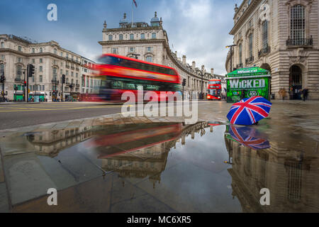 Londres, Angleterre - 03.15.2018 : Réflexion des autobus à impériale rouge en déplacement à Piccadilly Circus, avec la parapluie. Piccadilly Circus est le m Banque D'Images