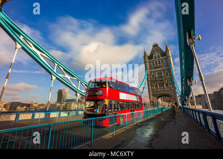 Londres, Angleterre - rouge iconique double-decker bus dans motion sur la célèbre Tower Bridge avec skyscraper de quartier des banques à l'arrière-plan. Ciel bleu et nuages Banque D'Images