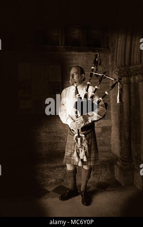 Image sépia d'un joueur de cornemuse écossais debout, en robe traditionnelle des hautes terres, jouant les cornemuses dans la porte de l'église Swalcliffe Oxfordshire Banque D'Images