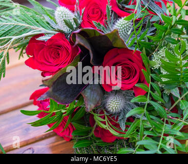 Mariage bouquet de roses rouges dans la verdure de chardons et d'autres portant sur une table en bois. Banque D'Images