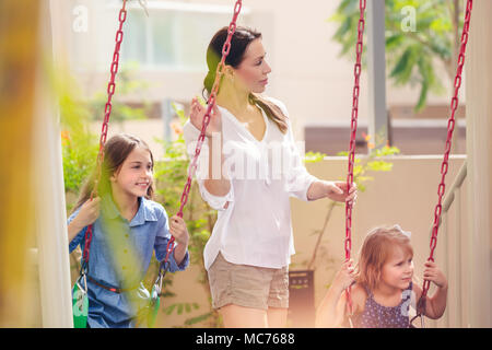 Mère de deux filles sur l'aire de jeux, de belles jeunes filles maman rocks son précieux sur la balançoire, heureux en famille week-end ensemble de dépenses Banque D'Images