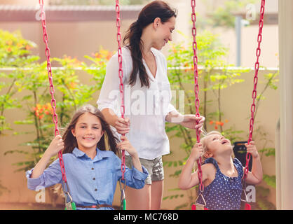 Mère de deux filles sur un terrain de jeux, de belles jeunes filles maman rocks son précieux sur l'oscillation, l'amusement pour les enfants, plein air famille heureuse spendi Banque D'Images