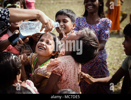 Une femme donne à l'eau Rohingya enfants pendant qu'ils jouent dans les champs voisins. Il y a maintenant environ 600 000 réfugiés Rohingyas dans le camp de réfugiés de Kutupalong le sud du Bangladesh. Alors que des préparatifs sont en cours pour la saison des pluies qui approche rapidement, de nombreuses ONG ont quitté laissant beaucoup de travail à faire pour compenser leur manque à gagner. Banque D'Images