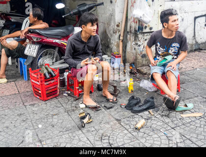 Deux hommes assis sur des tabourets en plastique la réparation de chaussures, travailler sur le trottoir dans une rue à Ho Chi Minh City, Vietnam. Banque D'Images
