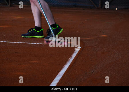 Homme en short de tennis de nettoyage des lignes d'angle avec un balai Banque D'Images