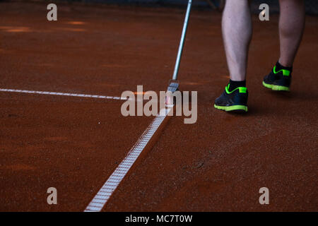 Homme en short de tennis de nettoyage des lignes d'angle avec un balai Banque D'Images