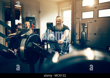 Mettre en place l'homme mature avec une barbe exerçant sur une machine à ramer pendant une séance de classe dans une salle de sport Banque D'Images