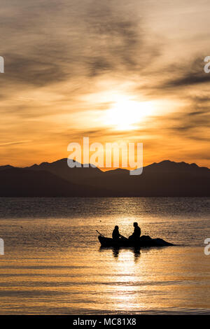 Silhouettes de deux hommes l'aviron dans un petit bateau de pêche à un lever du soleil d'or à Corfou, Grèce. Vertical image Banque D'Images