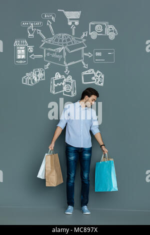 Cheerful man se sentir satisfait de son achat tout en maintenant les sacs en papier Banque D'Images