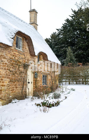 Thatched cottage en pierre dans la neige de l'hiver. Great Tew, Cotswolds, Oxfordshire, Angleterre Banque D'Images