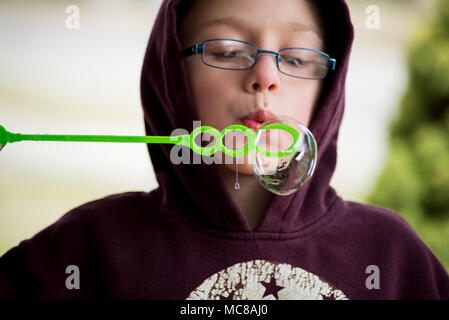 Un jeune garçon souffle bulles à l'appareil photo. Banque D'Images