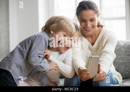 Smiling mother en tenant avec mignon selfies kids sur smartphone, heureux jeune mère rire faire photo avec petit-fils et sa fille à la maison, une maman unique Banque D'Images