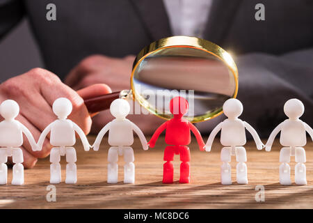 Close-up de l'homme d'affaires's Hand Holding Magnifying Glass sur Rouge Figure humaine sur un bureau en bois Banque D'Images