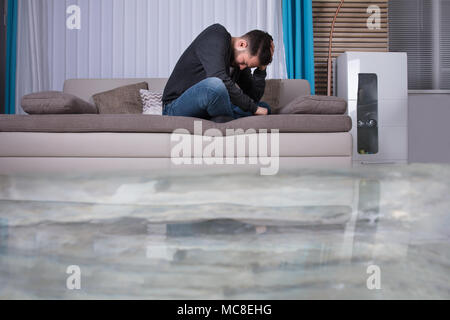 L'homme bouleversé sur canapé avec les mains sur la tête dans la pièce inondée avec de l'eau Banque D'Images