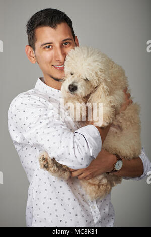 Smiling hispanic man holding poodle dog. Jeune homme avec l'animal Banque D'Images