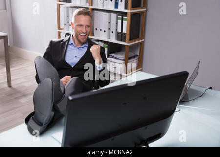 Excited Businessman Looking At Computer avec pieds sur Desk In Office Banque D'Images