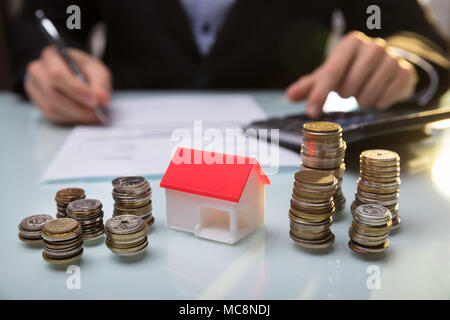 Modèle de maison et empilés sur des pièces de bureau en face de d'affaires travaillant sur le document Banque D'Images