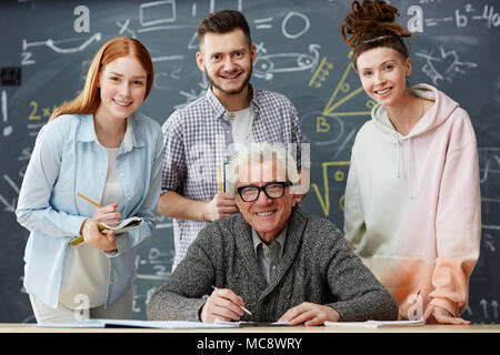 Heureux professeur et ses élèves à la réussite à l'appareil photo sur fond de tableau noir dans la classe Banque D'Images