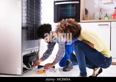 Femme à l'examen de technicien au réfrigérateur avec un multimètre numérique en cuisine Banque D'Images