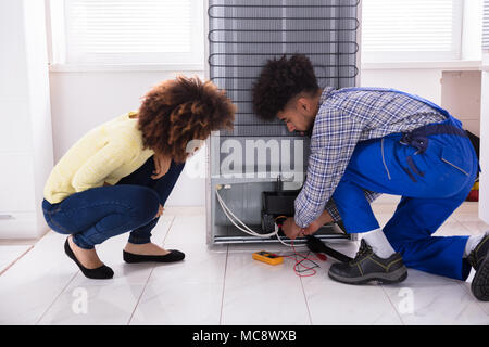 Femme à l'examen de technicien au réfrigérateur avec un multimètre numérique en cuisine Banque D'Images