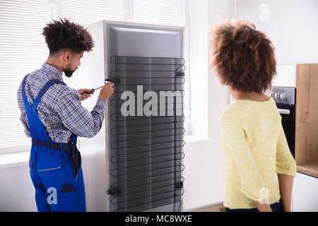 Technicien de réparation réfrigérateur à l'aide d'un tournevis dans la cuisine Banque D'Images