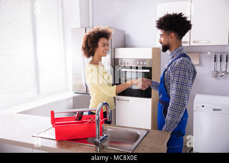 Réparateur en uniforme se serrer la main avec Young Woman in Kitchen Banque D'Images