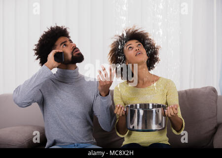 Jeune homme femme tout en appelant à l'aide plombier ustensile pour recueillir l'eau qui coulait du plafond Banque D'Images