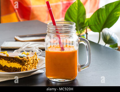 Délicieux gâteau au chocolat et smartphone avec verre de thé glacé ou de jus d'orange dans un café sur la table arrière-plan flou. Banque D'Images