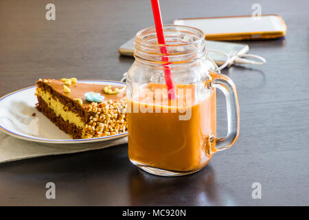 Délicieux gâteau au chocolat et smartphone avec verre de thé glacé ou de jus d'orange dans un café sur la table arrière-plan flou. Banque D'Images