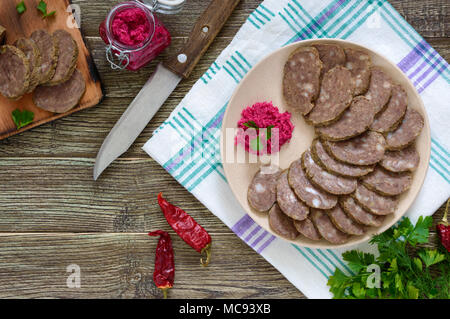 Diététique fait maison de la saucisse de foie sur une table en bois. Couper la saucisse en morceaux dans un plat avec sauce au raifort. Vue d'en haut. Banque D'Images