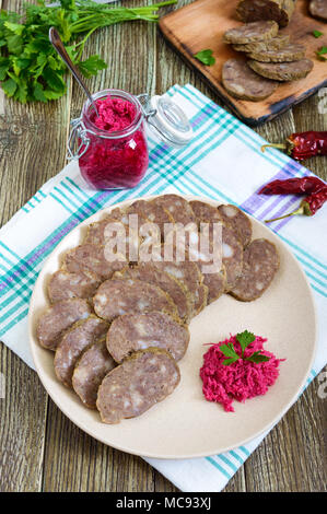 Diététique fait maison de la saucisse de foie sur une table en bois. Couper la saucisse en morceaux dans un plat avec sauce au raifort. Banque D'Images