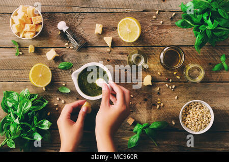 Femme mains rendant pesto italien dans un bol. - Ingrédients basilic, citron, parmesan, pignons de pin, ail, huile d'olive et de sel sur fond de bois rustique. Haut Banque D'Images