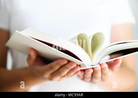 Jeune fille en T-shirt blanc lecture livre ouvert avec forme de coeur, love concept. Copier l'espace. Banque D'Images