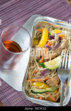 Chinois à emporter sauté de poulet et nouilles dans un plat de livraison d'aluminium avec un verre de Saki Banque D'Images