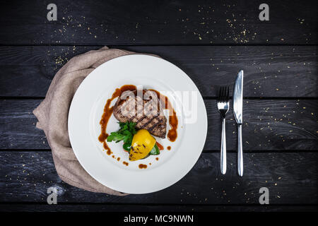 Steak de veau aux légumes grillés, servis sur la plaque blanche avec des couverts et de linge de maison serviette, sur le fond de bois. Vue d'en haut. Banque D'Images