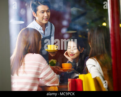 Les jeunes femmes asiatiques waiter serving clients dans un café, d'une balle dans la fenêtre en verre. Banque D'Images