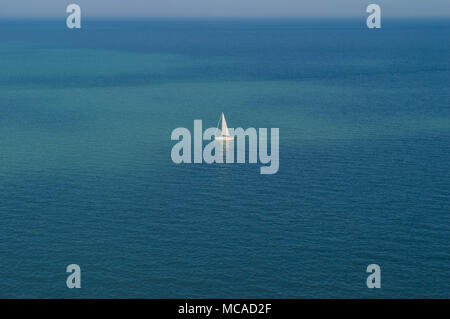 Un yacht à voile blanc au centre de l'image au milieu de la mer bleue.L'horizon est en haut de la trame et la mer est bleu clair et turquoise. Banque D'Images