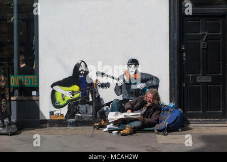 Un homme se détend sur la chaussée à Soho en face d'une photo de John Lennon et Paul McCartney Banque D'Images