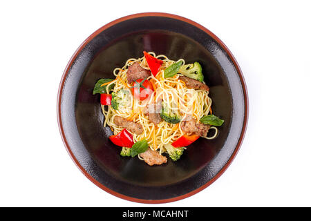 Les nouilles aux oeufs avec du porc dans la sauce teriyaki, isolé sur fond blanc. Les nouilles aux oeufs dans une plaque noire. Assiette de forme inhabituelle. Banque D'Images