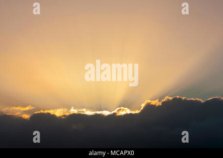 Rayons de soleil d'or sortant de derrière un nuage sombre au coucher du soleil Banque D'Images